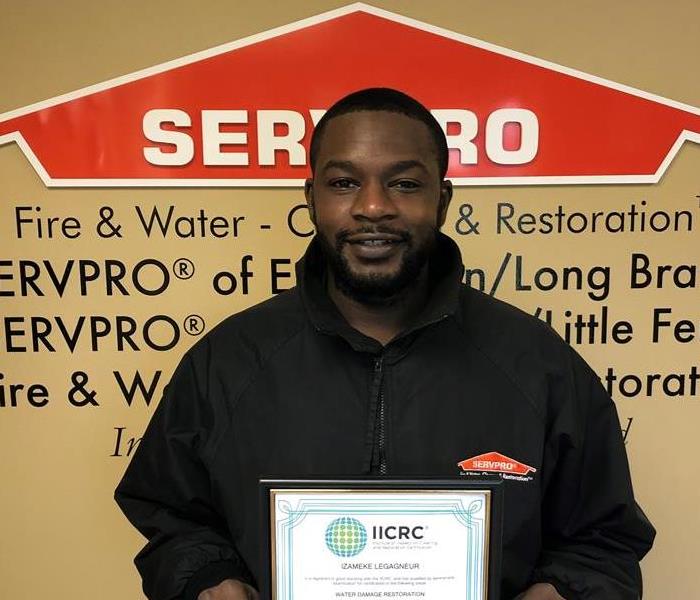 Team member, Meek, standing in front of SERVPRO logo with IICRC certification 